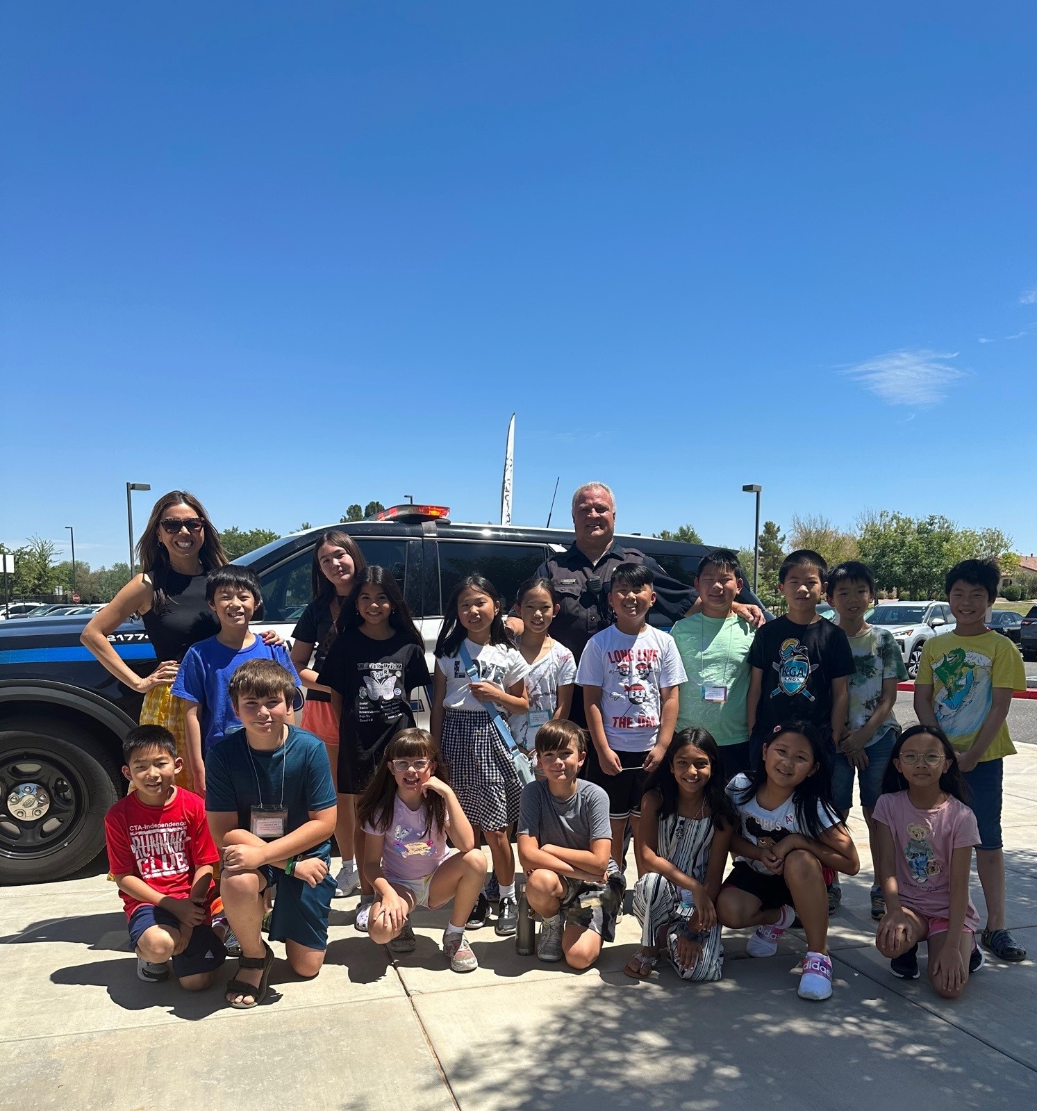 Image of class of students smiling with a Chandler police officer and their teacher in front of a police car